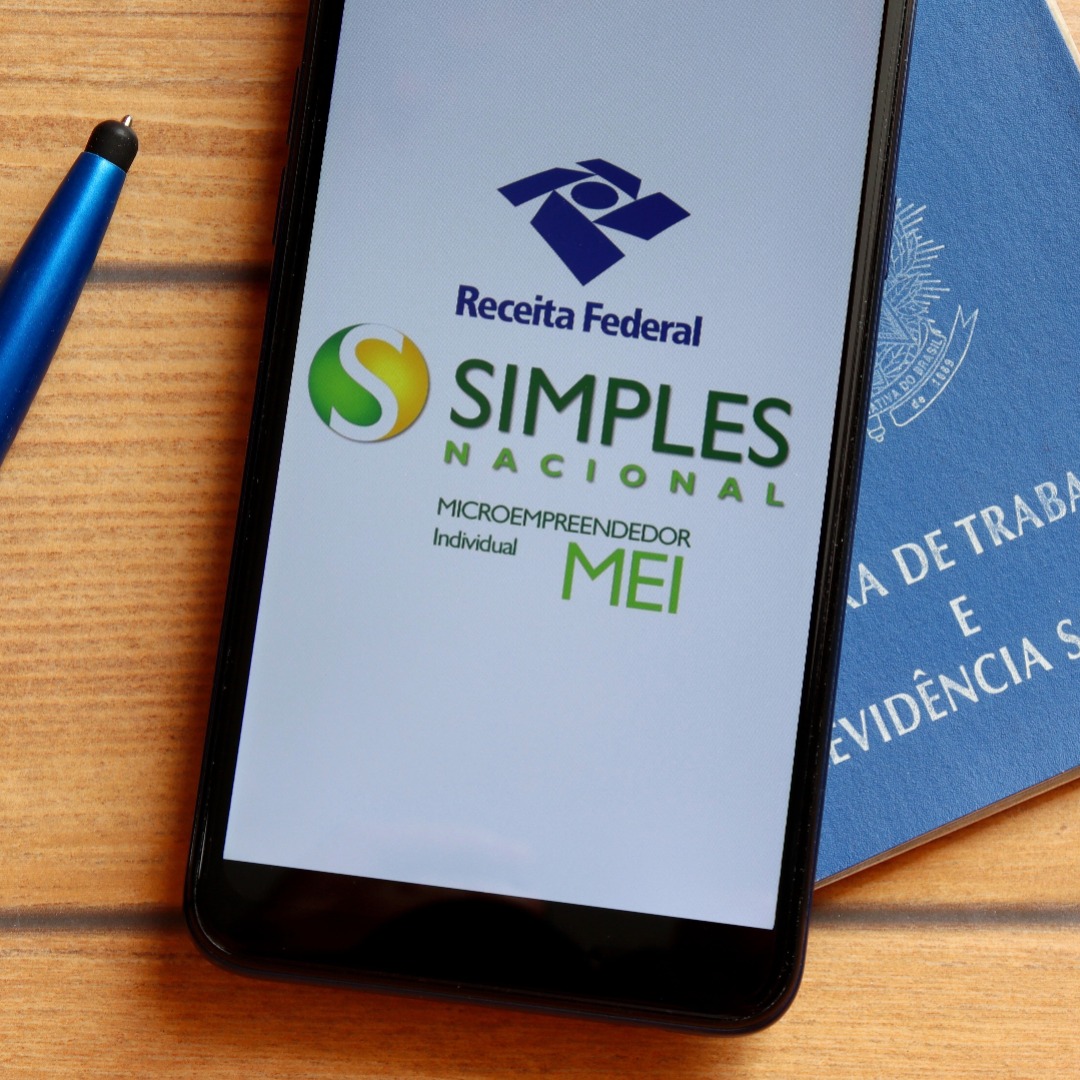 Imagem de celular exibindo o sistema do Simples Nacional para MEI e imagem da carteira de trabalho e previdência social ao lado.
